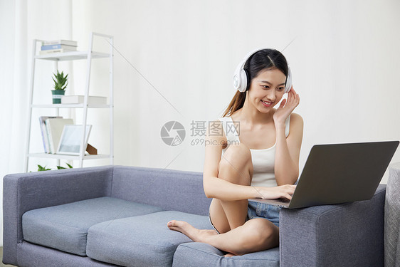 居家青年女性戴着耳机使用笔记本电脑图片