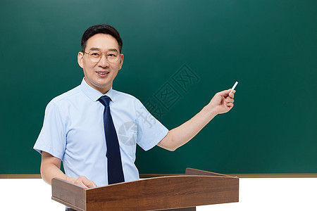 中年教授手拿粉笔站在黑板前讲课图片