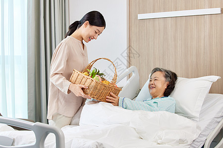 手拿果篮的女性探望生病住院的老人背景图片
