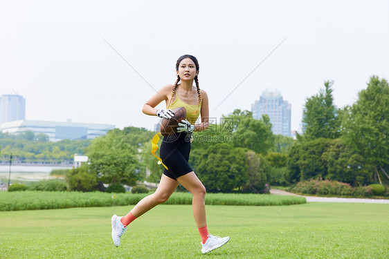 年轻美女抱着橄榄球奔跑图片