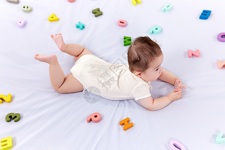 可爱婴儿趴在铺满字母的床上背景图片