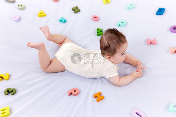 可爱婴儿趴在铺满字母的床上图片
