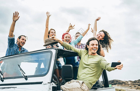 一群快乐的朋友在吉普车上用智能手机自拍年轻人在公路旅行中玩得开心友谊假期青年假期图片