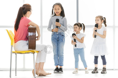 亚洲老师坐在椅子上弹原声吉他教亚洲孩子唱歌图片