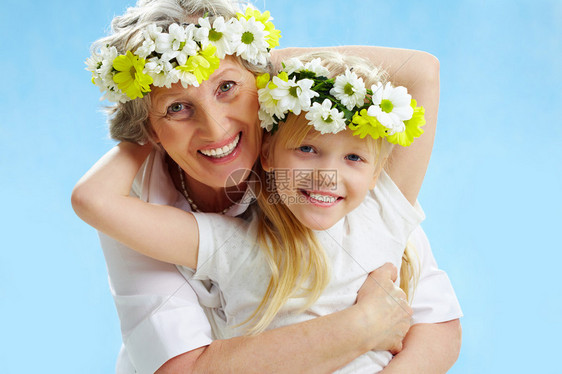 戴着花环的外祖母和孙女在蓝背景上拥抱图片