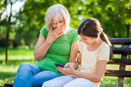 祖母和孙女坐在公园里使用手机图片