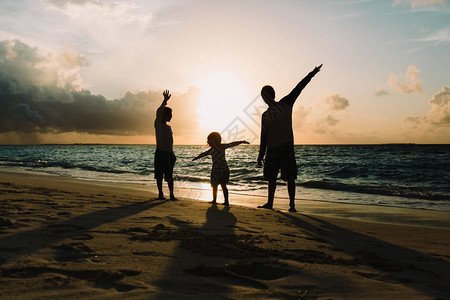 父亲带着小儿子和女儿剪影在日落海滩玩耍图片