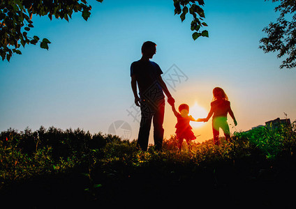 父亲和两个女儿在日落时走图片