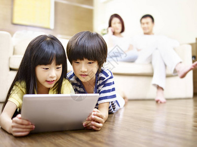 两名亚裔儿童躺在地板上玩电子游戏图片