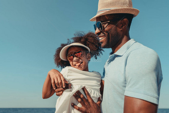 快乐的非洲美国父亲和女儿戴着墨镜在海边玩得图片