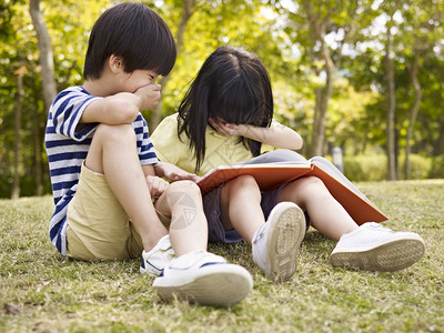在公园户外看书时坐在草地上大笑着的小图片
