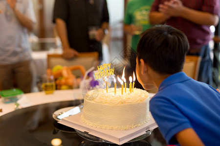 年轻男孩庆祝生日和家人一起在蛋糕上吹蜡烛图片