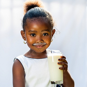 可爱的非洲小女孩喝牛奶的近距离肖像在光线背景下孤立无援图片