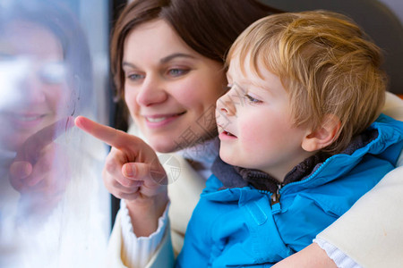 快乐的年轻母亲和蹒跚学步的小男孩在火车行驶时透过窗户向外看图片