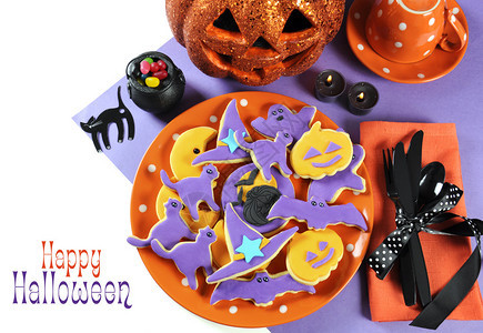 橙色圆点板上的帽子蝙蝠和南瓜形状的万圣节快乐橙色和紫色糖饼干图片