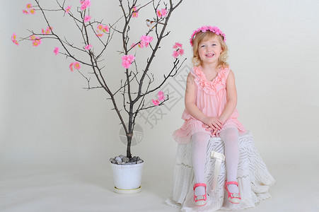 女孩在一个粉红色的花圈和粉红色的连衣裙与开花树上背景图片