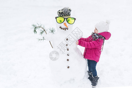 快乐的小女孩平原一个雪人戴眼镜在雪图片