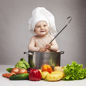 小男孩在厨师的帽子与酱锅和不同的蔬菜在黑图片