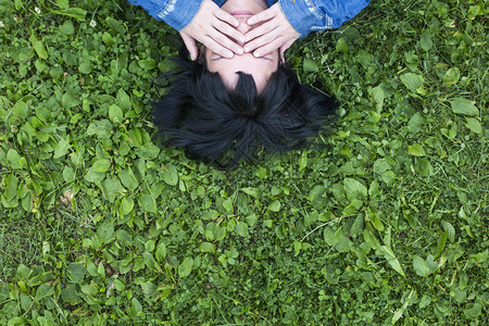 黑发女孩躺在草地上双手闭上眼睛顶视图片