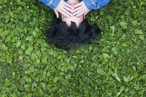黑发女孩躺在草地上双手闭上眼睛顶视图片