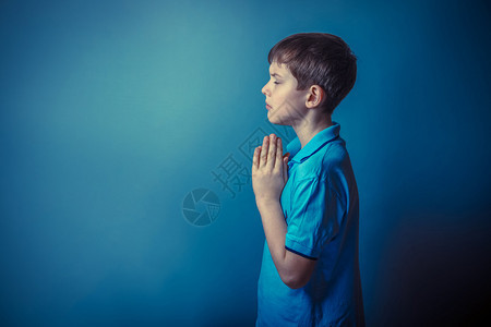 十年的欧洲青少年外表站在侧面祈祷在灰色背景图片
