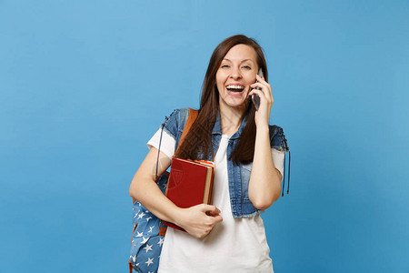 年轻的笑女学生背着包拿着课本在手机上交谈图片