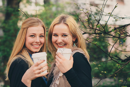两个漂亮的女孩拿着咖啡露出自信的笑容图片