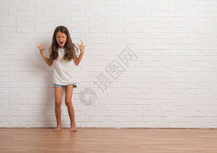 年轻的西班牙小孩在白砖墙上挥舞着疯狂的表情喊叫图片