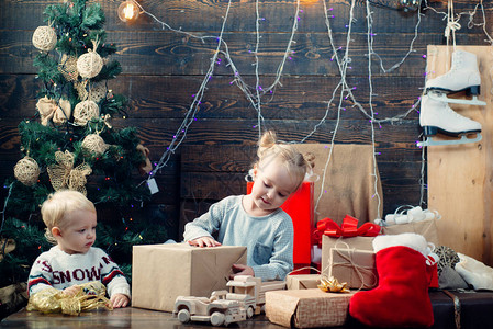 快乐的孩子在圣诞树旁看着装饰玩具球的画像戴着圣诞帽的快乐小孩带着礼物过圣诞节圣诞节快乐圣诞节前的早晨图片