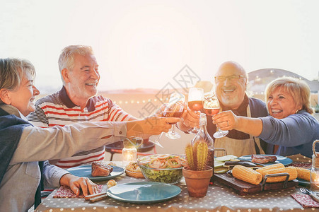 快乐的老朋友在户外露台烧烤时用红酒欢呼快乐成熟的人做晚餐敬酒眼镜和一起笑友谊和老年人生图片