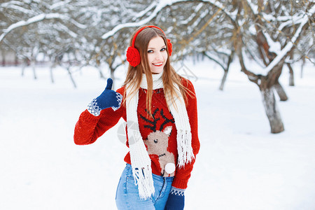 穿着红色毛衣的年轻美女带着驯鹿和冬季耳机在公园玩得开心图片