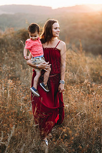 穿着红色长裙的漂亮年轻妈带着年幼的儿子轻松地散步图片