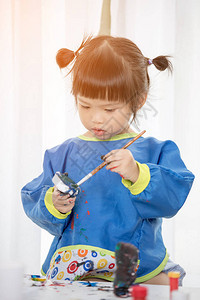 一个可爱的小女孩在乱七八糟地玩颜料的肖像图片