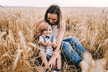 美丽的母亲和年轻的儿子坐在小麦田图片