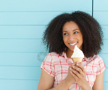 一个可爱的年轻女子在户外蓝背景微笑和吃冰淇淋图片