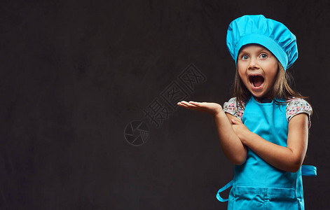 穿着蓝色厨师装扮成演播室的小女孩很惊讶孤立在黑暗图片