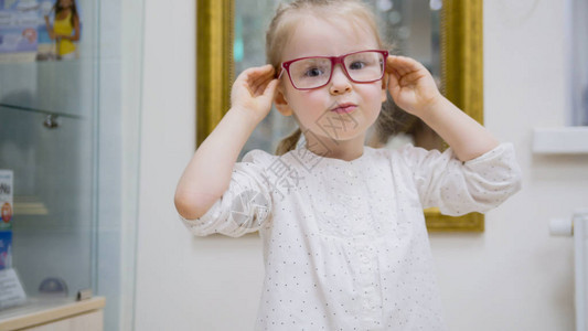 小女孩在镜子旁边试戴时装医疗眼镜在眼科诊所买图片