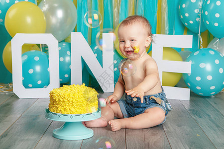 可爱的白种人男婴在牛仔裤子庆祝他的第一个生日的肖像蛋糕粉碎概念坐在工作室地板上的小孩吃着美图片