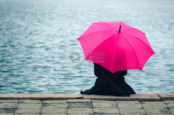 寂寞的女人坐在粉红色的雨伞旁图片