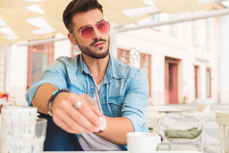 身穿蓝衬衫和墨镜的闲男在城里喝咖啡的人看着面图片