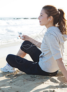 一位年轻女子坐在细沙海滩岸边的侧面肖像视图图片