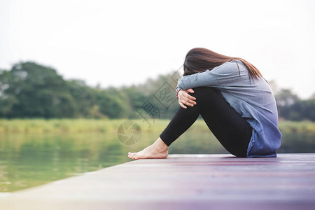 在WoodenPatioDeck河边坐在河边的伤痛妇女图片