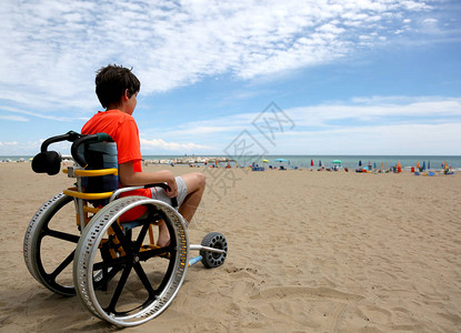男孩在特殊的轮椅上夏天沙滩上图片