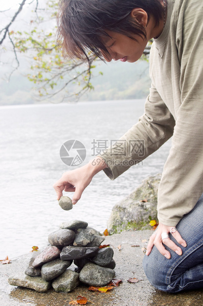 一个年轻迷人的亚洲日本男子在雨天在户外建造一个美丽的湖泊和山脉景观的岸边的石头金字图片