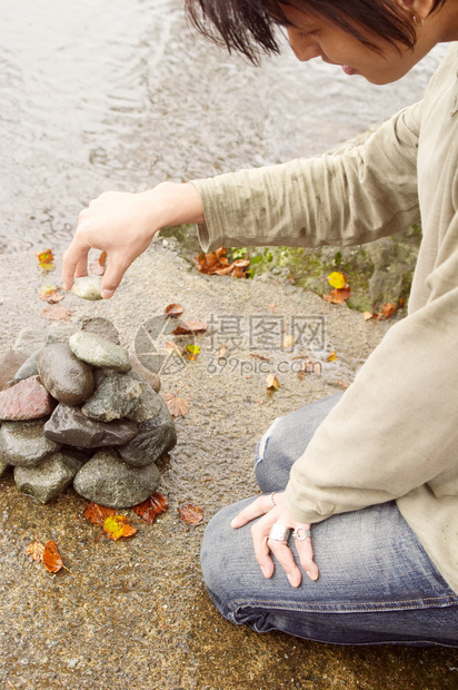 一个年轻的有吸引力的亚洲日本人在雨天在户外建造一个美丽的湖景岸边的石头金字塔桩图片