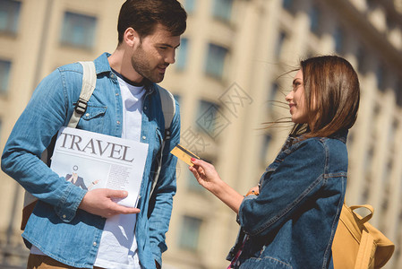向手持旅行报纸的男朋友发放信用卡的时髦女游客图片