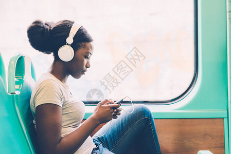 使用智能手机乘公共汽车旅行的年轻黑人女听音乐图片