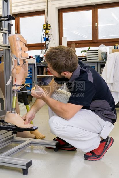 年轻男技师使用工具在实验室调整假肢腿组装的膝盖部位图片