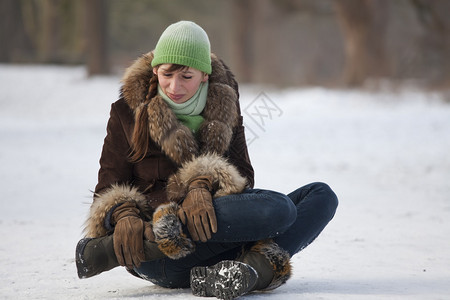 疼痛的女人在雪路上滑倒后抱住膝盖图片