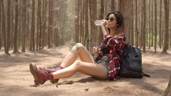 年轻快乐的背包女孩在步行旅自然和冒险旅行后坐在休息瓶里喝水图片